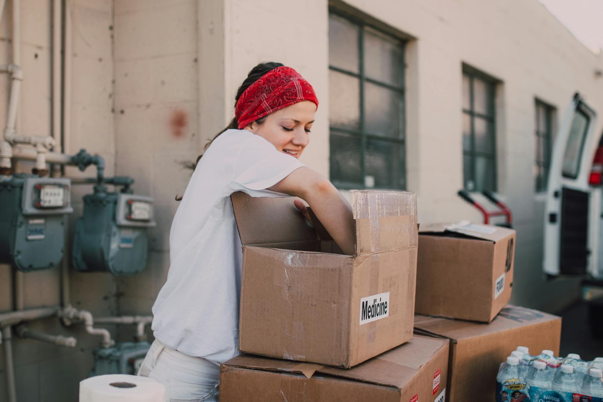 A woman volunteer sorting medicine boxes for charity donations outdoors.